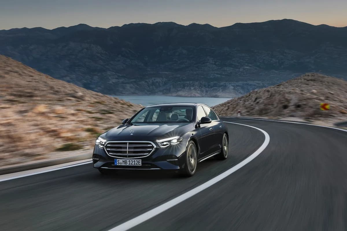 Mercedes-Benz Classe E de Kotewo en action sur une route sinueuse de montagne, illustrant sa polyvalence et son dynamisme. Cette berline luxueuse fait partie de notre gamme de véhicules premium aux côtés des Mercedes Classe S, Classe V et Classe C, assurant vos déplacements en tout confort dans la région Rhône-Alpes. Sa silhouette élégante noire et ses technologies de pointe garantissent un voyage d'exception, que ce soit en ville ou sur les routes de montagne.