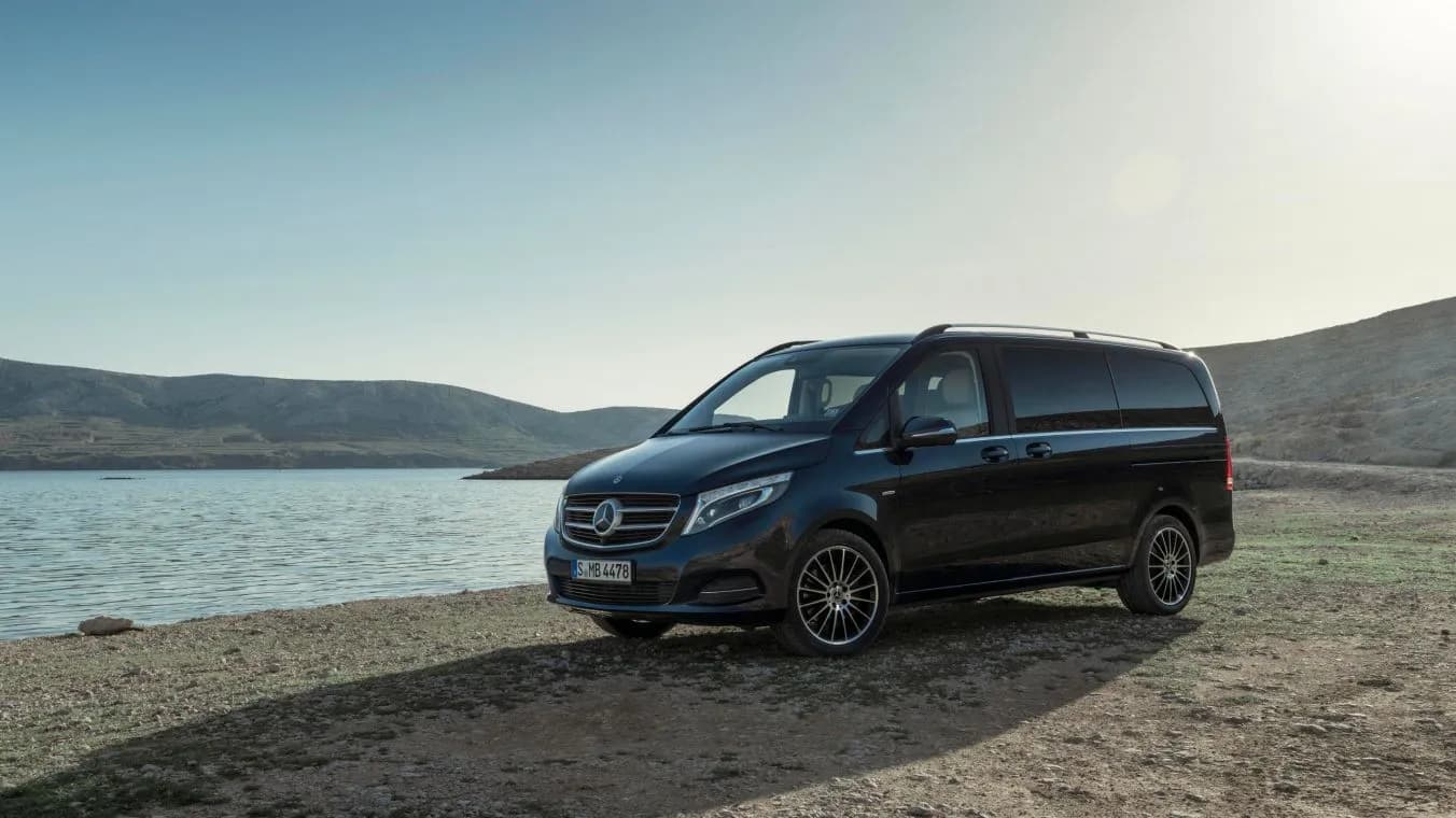 Mercedes-Benz Classe V de Kotewo photographié au bord d'un lac de montagne, illustrant sa polyvalence pour les transferts de groupes en tout confort. Ce van haut de gamme complète notre flotte de véhicules premium comprenant les Mercedes Classe S, Classe E et Classe C, idéal pour les déplacements professionnels ou familiaux en région Rhône-Alpes. Sa finition noire élégante et son habitacle spacieux permettent d'accueillir jusqu'à 7 passagers dans des conditions de confort optimales, que ce soit pour des trajets urbains ou des excursions en montagne.